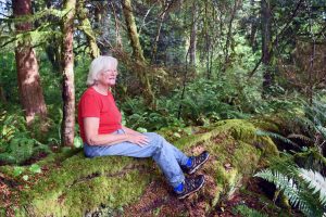 Janet Strong relaxes on the root of a hemlock tree on her property near McCleary, WA. Photo credit: Paul Dunn.