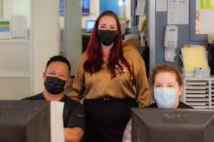 Nicole Simons standing behind two nurses sitting at desks