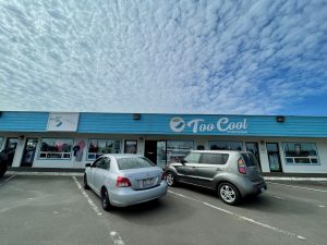 outside of Too Cool Sportswear in Ocean Shores with two cars parked out front