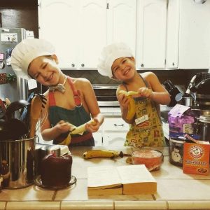two little boys in aprons and chef hats at a kitchen counter with bananas in their hands