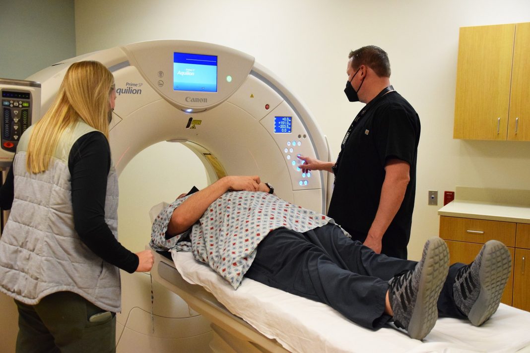 a person lying on a CT scanner with technicians standing on either side