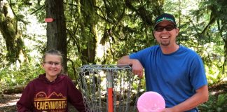 a man and child holding discs by a basket at the The Evergreen State College disc golf course