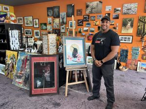 an artist stands by his paintings at the Fusions ART Gallery