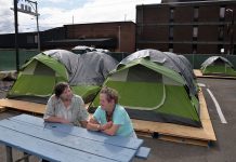 two people sitting at a picnic table with tents behind them