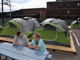 two people sitting at a picnic table with tents behind them