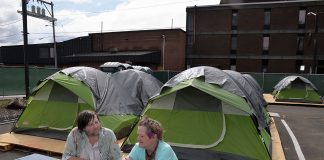 two people sitting at a picnic table with tents behind them