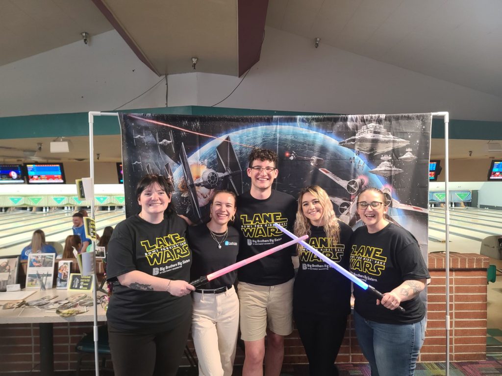 FASA employees with "Lane Wars" tshirts on and two of them holding lightsabers at a bowling alley