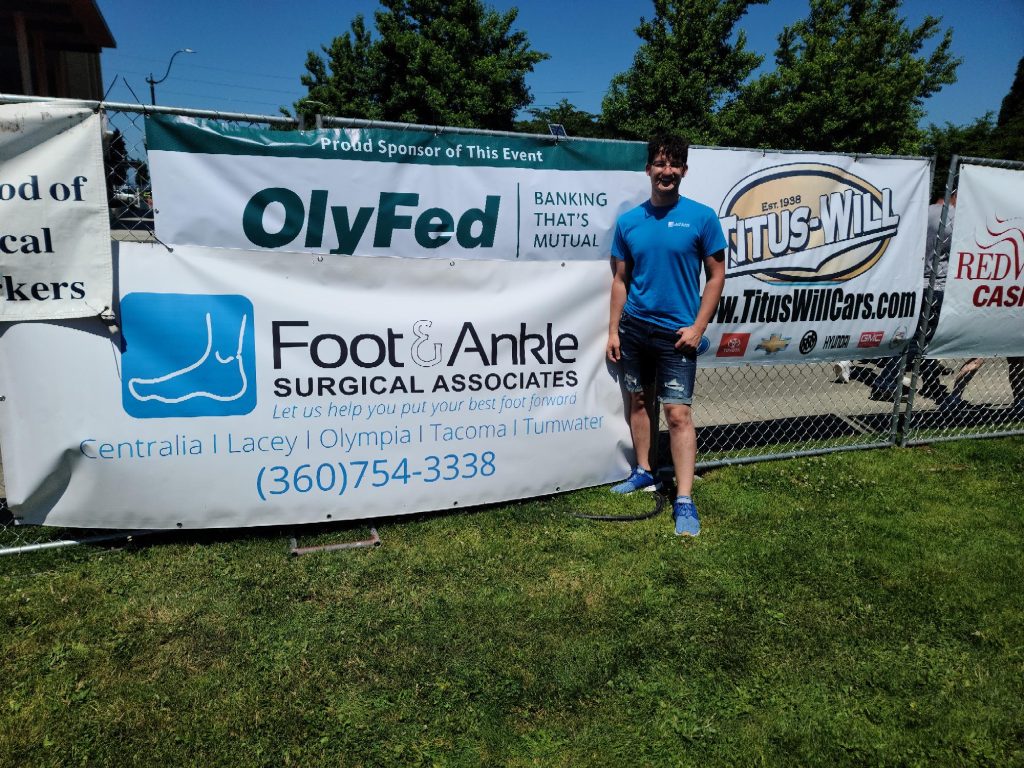 a person standing next to a Foot & Ankle Surgical Associates banner at an event outside in the grass