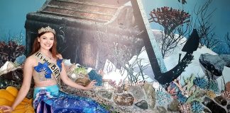 a woman dressed as a mermaid sitting in front of a sunken ship backdrop