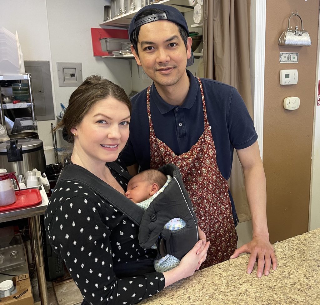 Thian’s Thai Fusion Owner Gretchen Dickson holding her son, standing next to, her husband, Boy Pakapongpun in their restaurant.