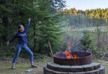 Lucky standing with her feet spread apart, one had stretched down and one stretched up in front of a large metal fire pit in the woods.