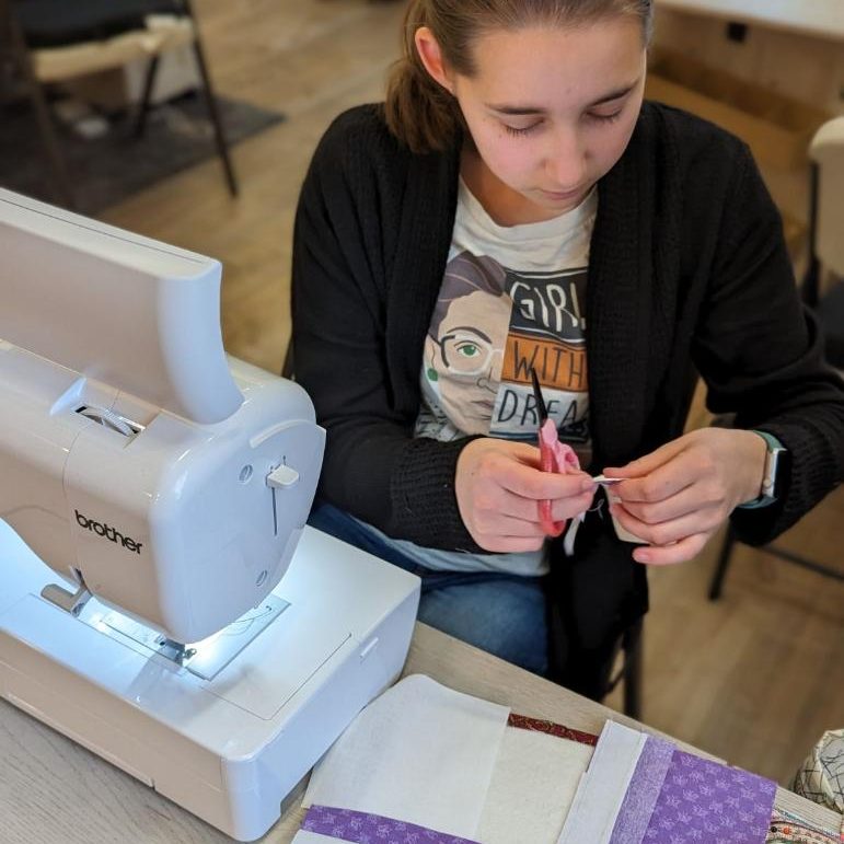 Lucy sitting at a table with a sewing machine, working on quilt blocks