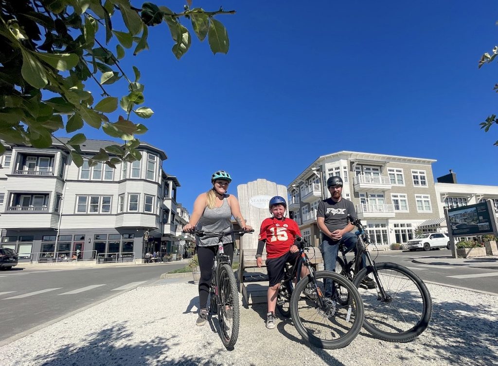 a man, woman and child post on their bikes in front of a Sebrook sign