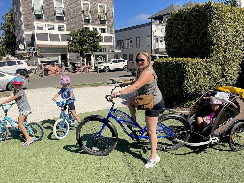 a woman with a bike pulling a child in a trailer and two older kids on bikes in front of her on a path in Seabrook