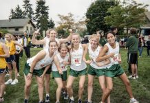 female runners in green shorts and white tank tops that say, 'Evergreen' pose for a photo.
