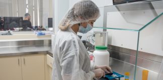 A person in scrubs, hair net and mask works on pills in a pharmacy