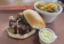 pulled pork sandwich on a tray with a cup of coleslaw and peach cobbler next to it
