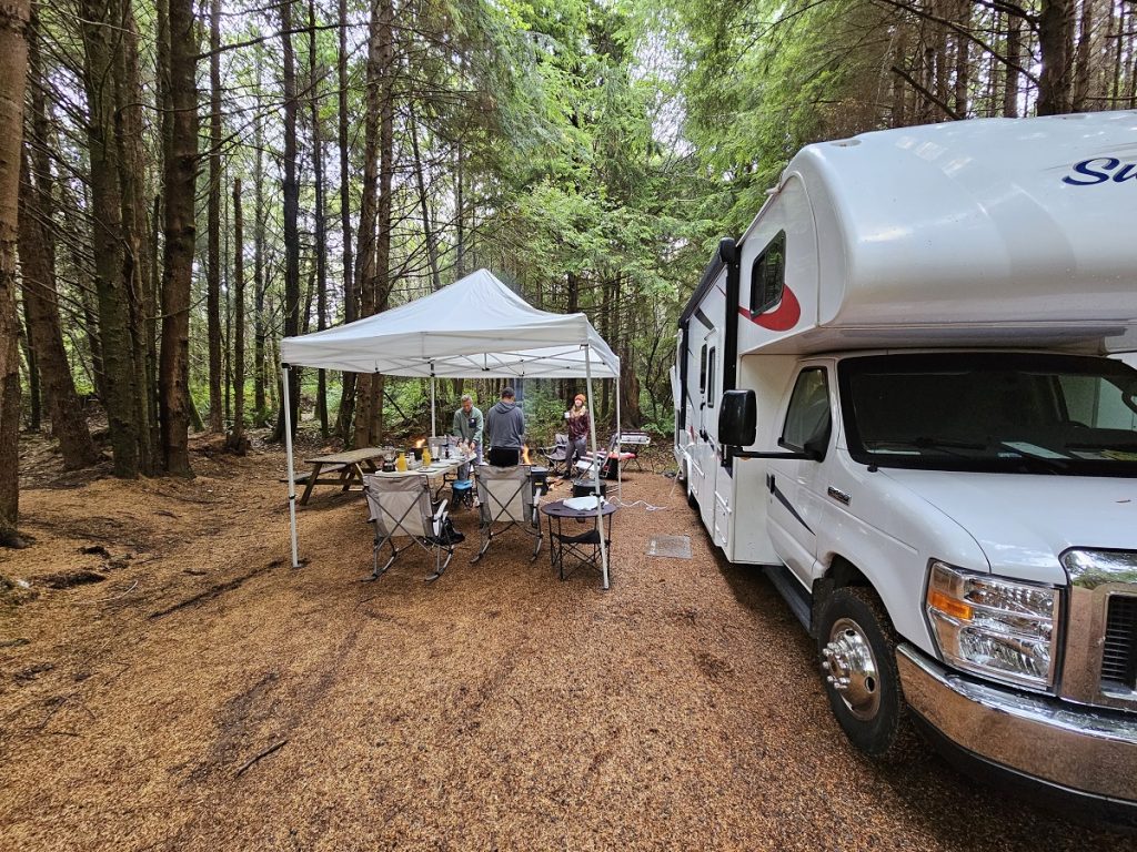 RV with a pop up tent and camping supplies in the woods