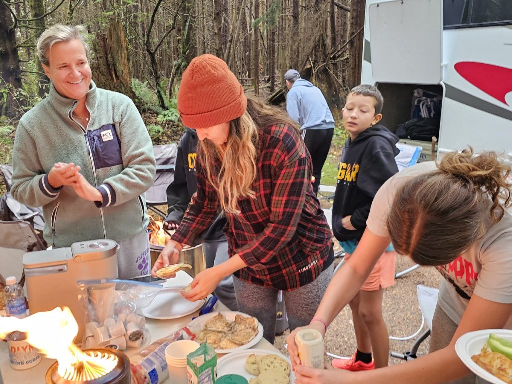 women and kids getting burgers and buns off a table in the woods