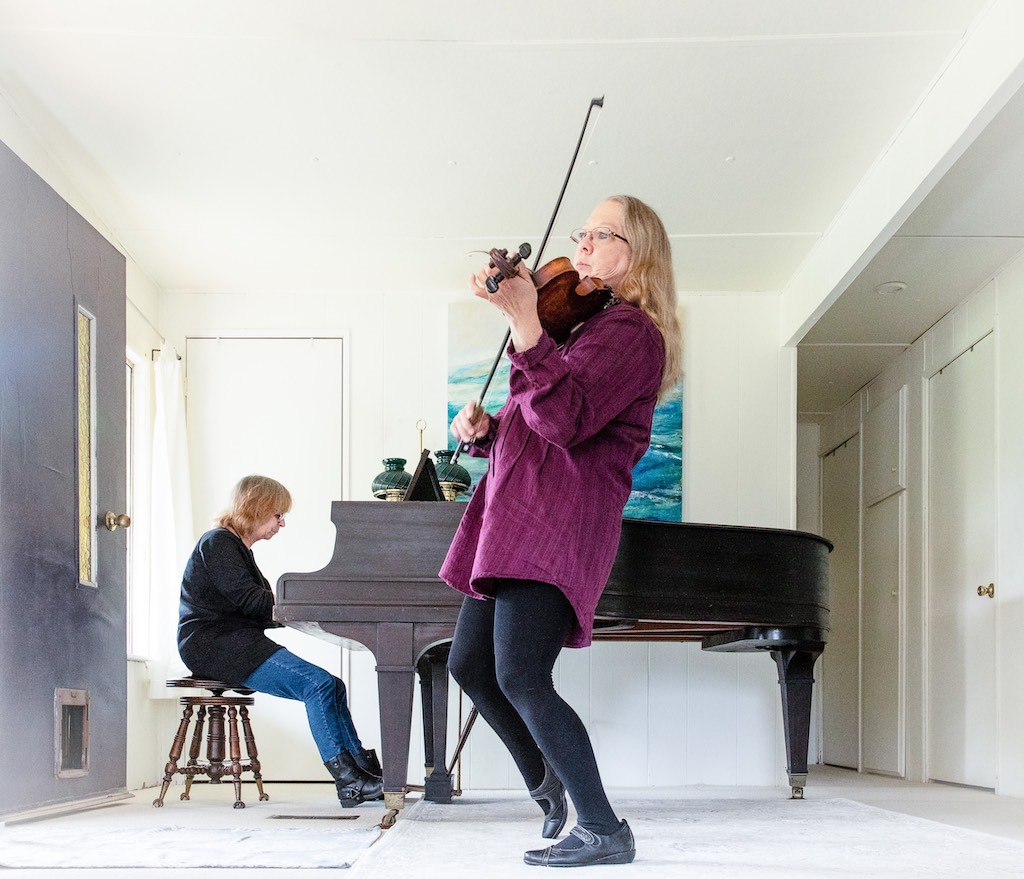 a man at a piano and a woman playing a fiddle inside a white room
