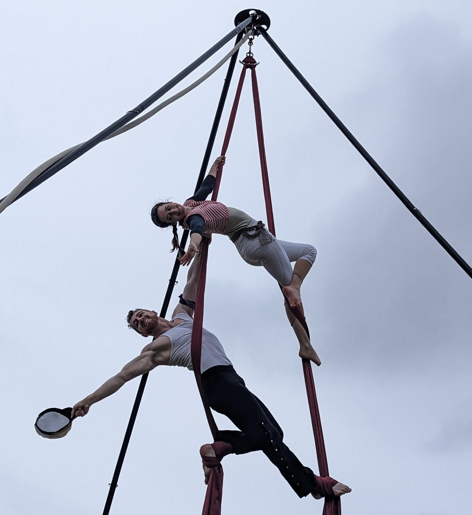 a ma and woman suspended in the air by ropes, holding each other's hand.