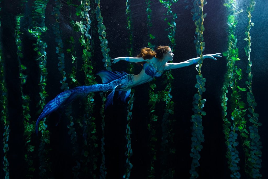 woman dressed as a mermaid swimming through kelp