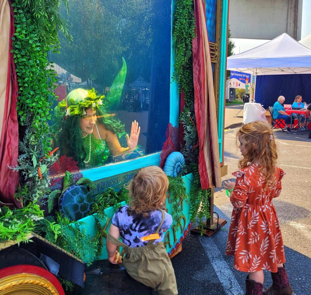 two little girls visit a woman dressed as a mermaid who is in a tank full of water