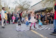 Kids dancing on a black-and-white checkered mat with a crowd around them on the street in downtown Olympia