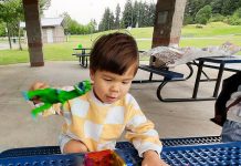 kid playing with colorful plastic shapes at a blue metal table under a park shelter