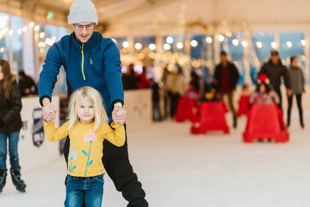 a man holds a girl by the arms in front of him while they ice skate