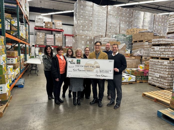 Bank-of-the-Pacific-Grant-Awards-Thurston-County-Food-Bank a large group of people stand around a giant check inside a warehouse