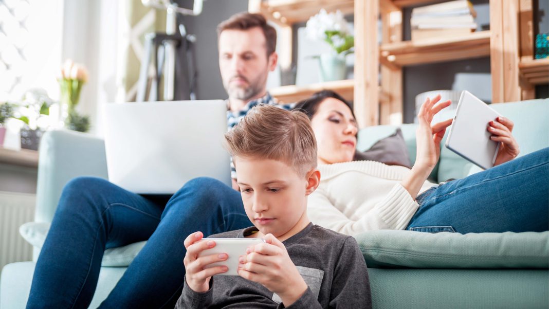 a man, woman and child, in a living room all on computer, tablets or phones